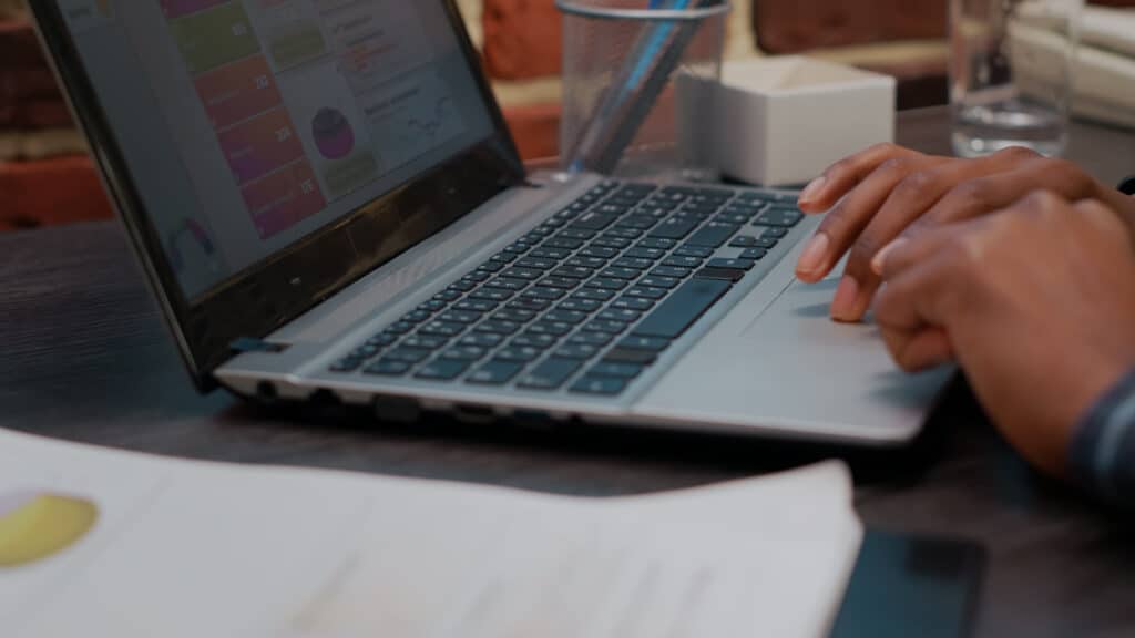 A person typing on a laptop with charts displayed on the screen, and some documents and a pen holder nearby—highlighting Why Accurate Transcripts Matter in Litigation for organizing essential case details.