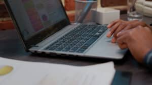 A person typing on a laptop with charts displayed on the screen, and some documents and a pen holder nearby—highlighting Why Accurate Transcripts Matter in Litigation for organizing essential case details.